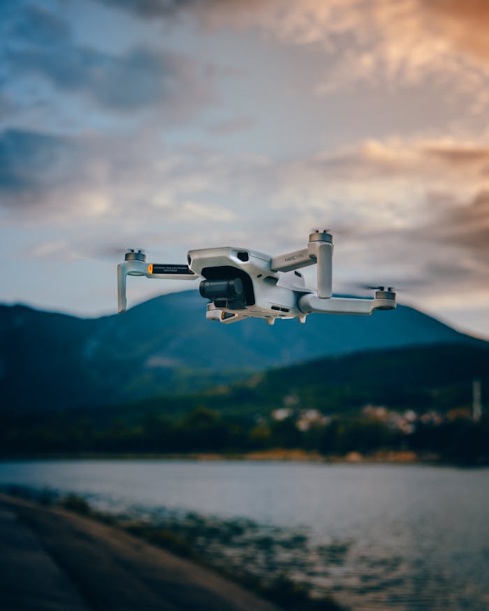 A white drone flying over a mountain lake with beautiful sunset clouds, showcasing nature and technology.